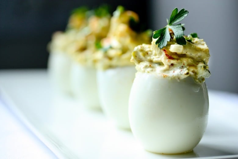 A simple delicious recipe for the Best EVER Deviled Eggs- Made with crumbled bacon, cheddar and onion. | www.feastingathome.com