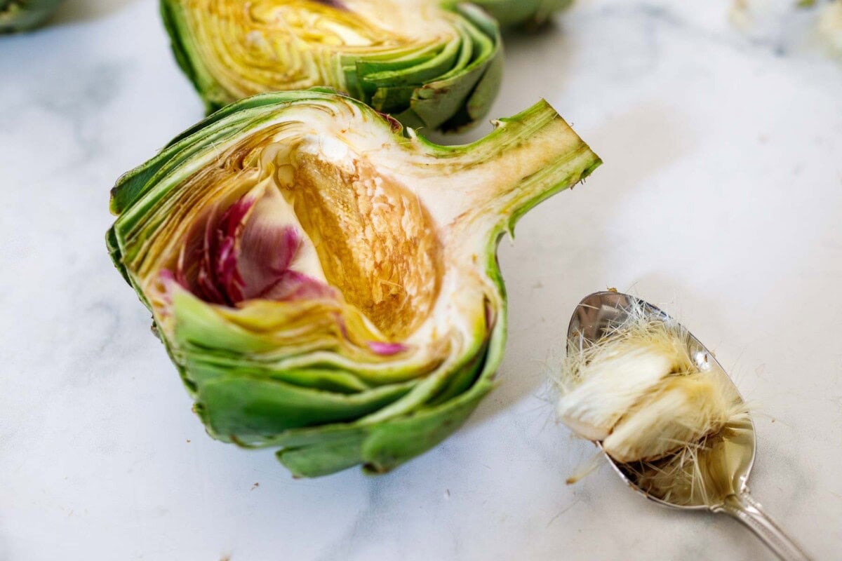 fresh artichoke cut in half with spoon that scooped out hairy center.