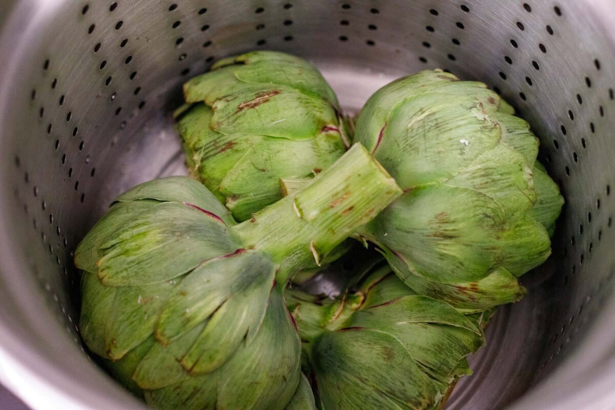 fresh artichoke halves face down in steamer basket.