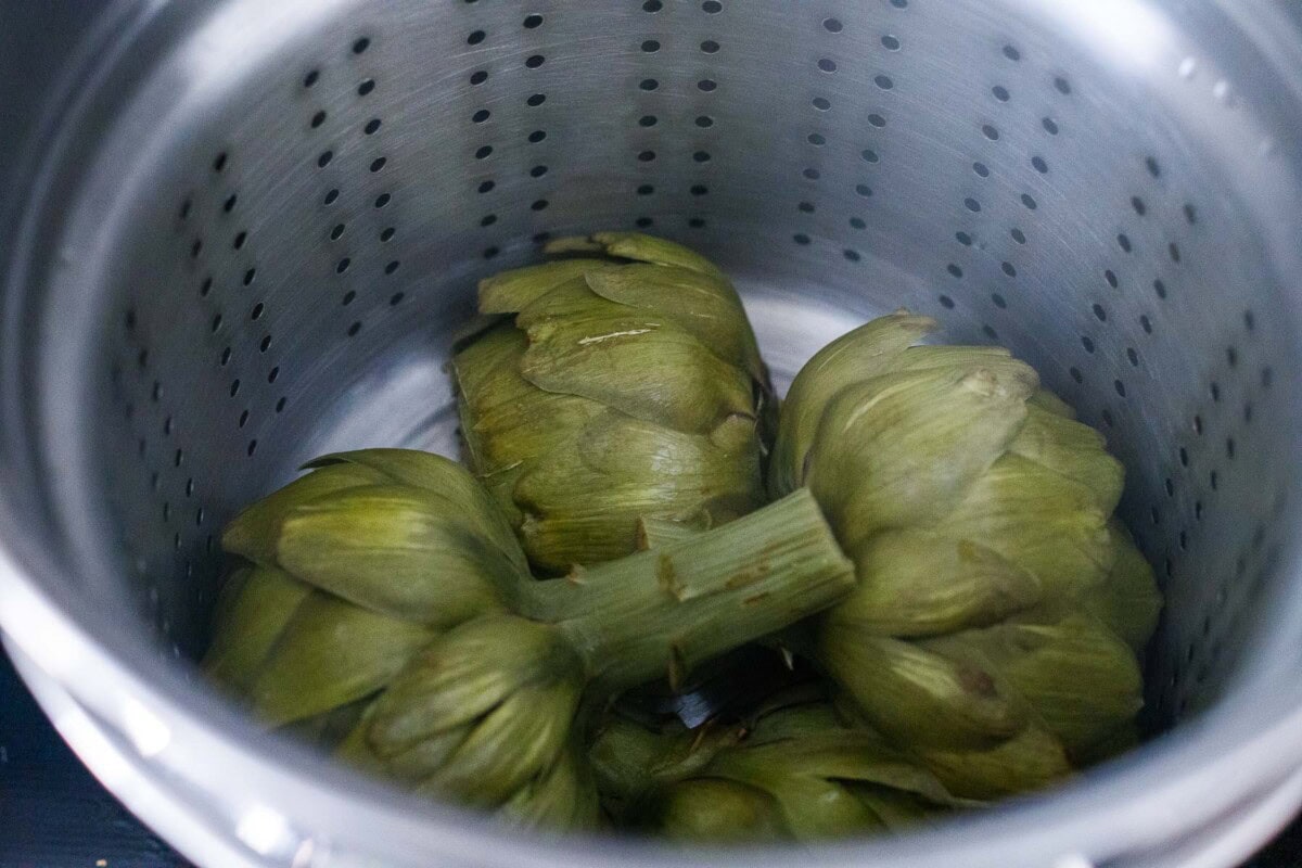 steamed artichoke halves face down in steamer basket.