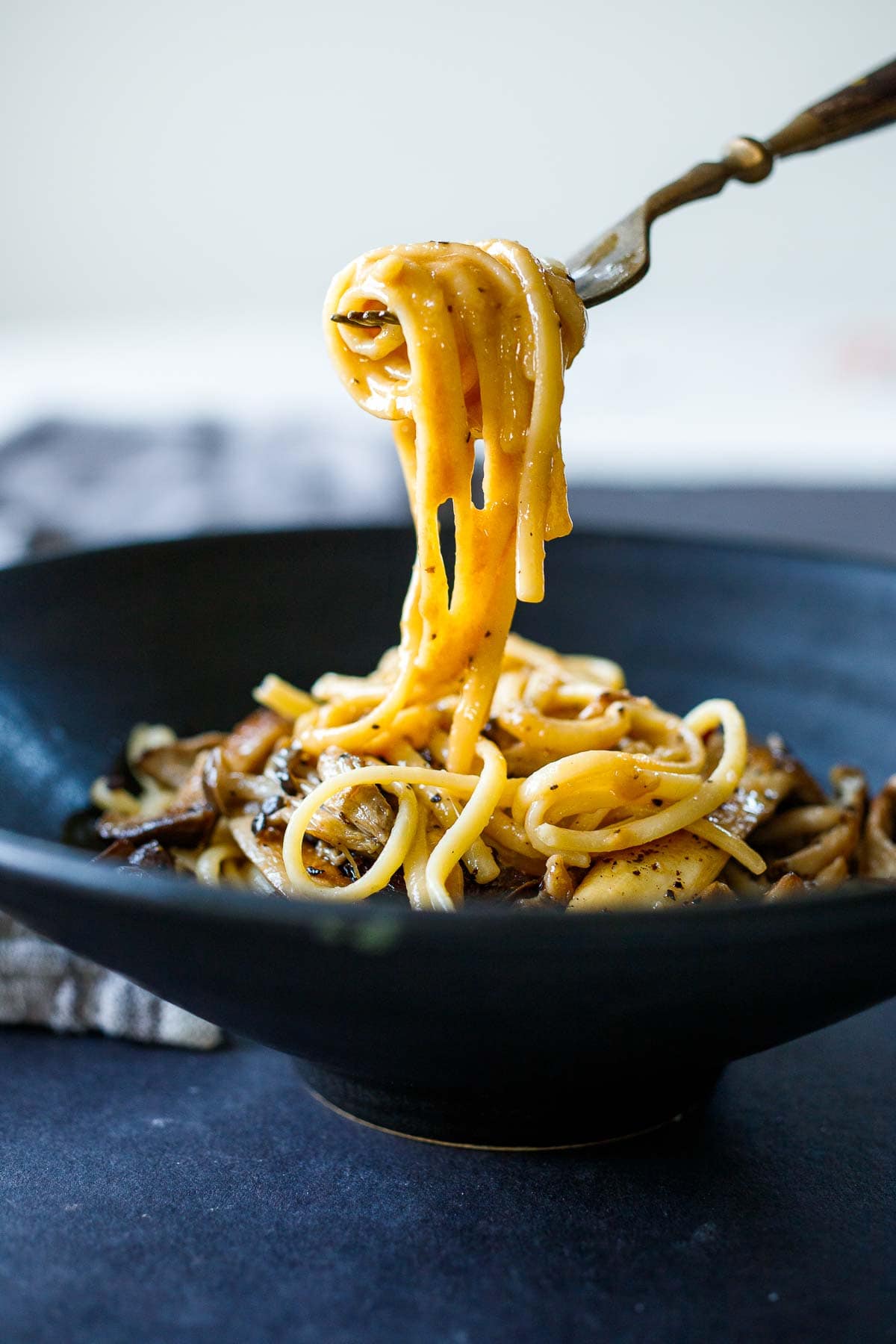 Creamy noodles being lifted out of a black pasta bowl with a fork. 
