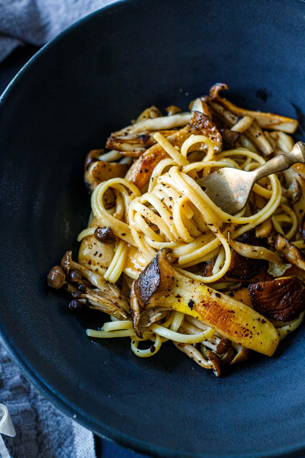 Creamy noodles topped with sauteed mushrooms in a black bowl. 