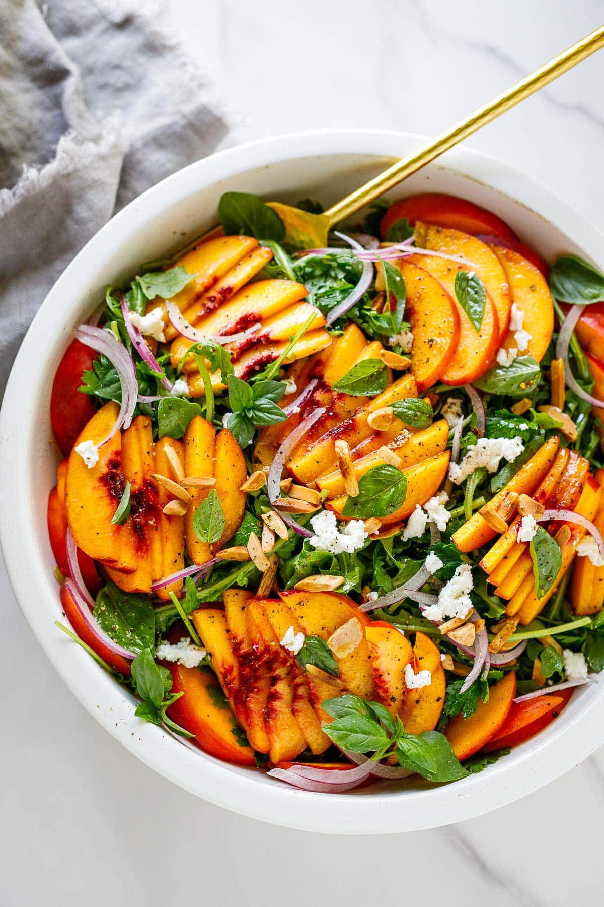 peach salad in a white bowl with arugula.