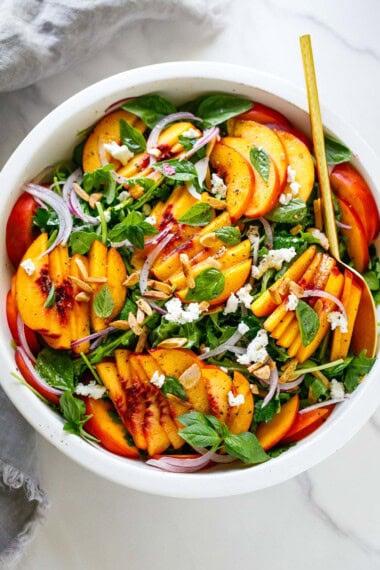 This summery peach salad recipe is made with fresh peaches, arugula, creamy goat cheese, slivered almonds, and basil tossed in a vinaigrette.