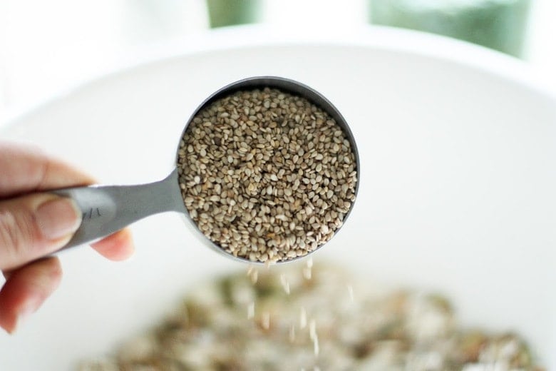 pouring sesame seeds into large mixing bowl to make healthy homemade granola recipe.