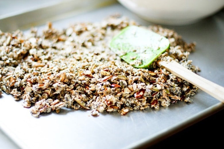 spreading out granola on baking sheet with a spatula.