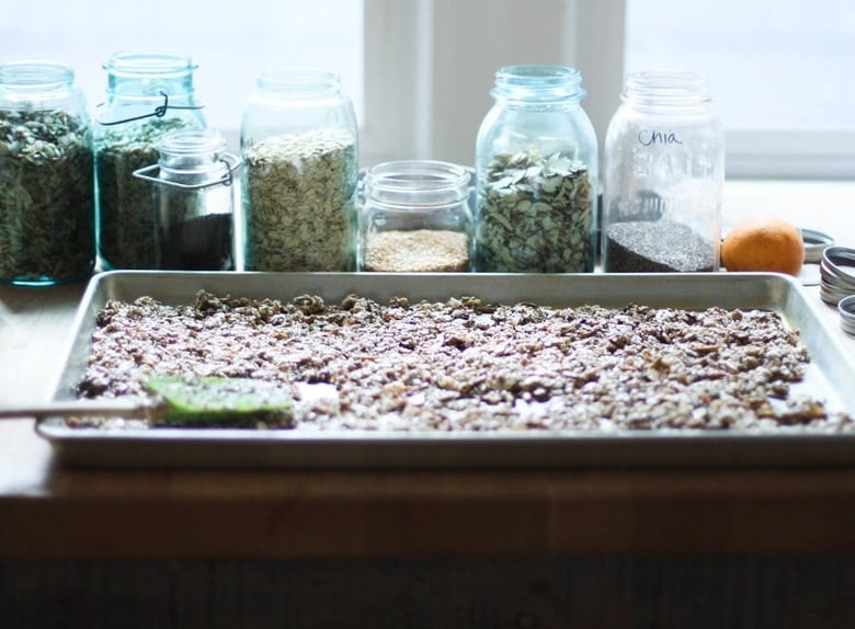 homemade granola spread out on baking sheet, using spatula to flatten it out.