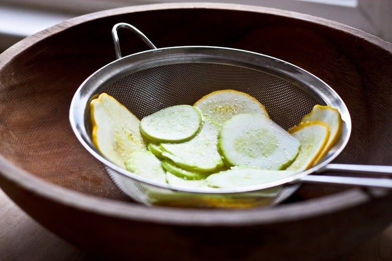 salting the zucchini in a strainer over a large mixing bowl.