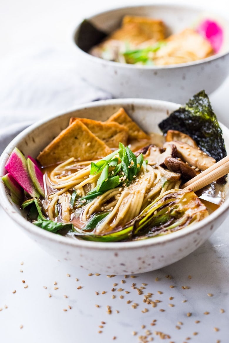 bowl of vegan ramen with noodles, bok choy, scallions, watermelon radish, crispy tofu, shiitake mushrooms, kombu, and sesame seeds.
