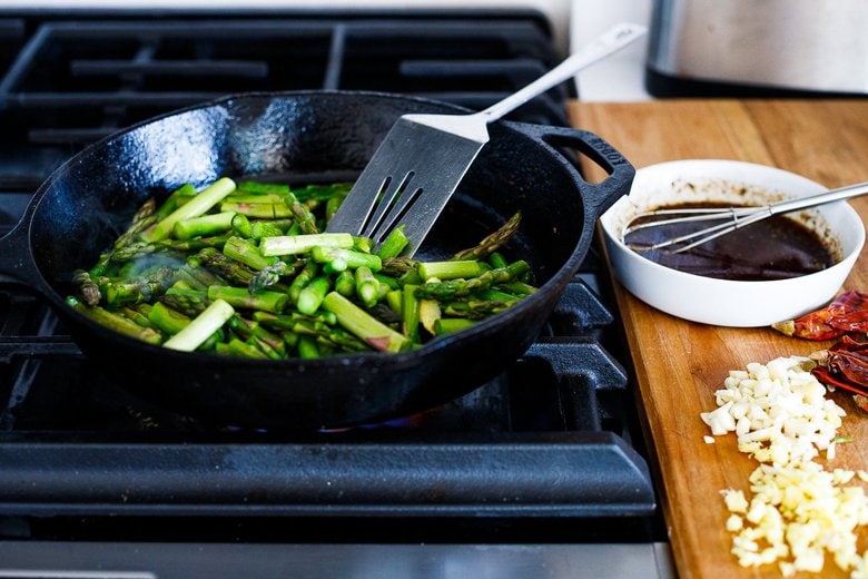 stir-frying asparagus with ingredients by the stove