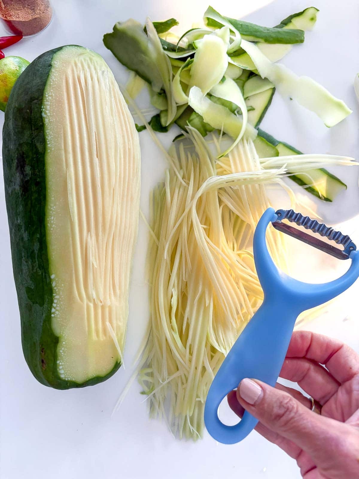 green papaya with hand holding a shredding tool, next to a pile of shredded papaya. 