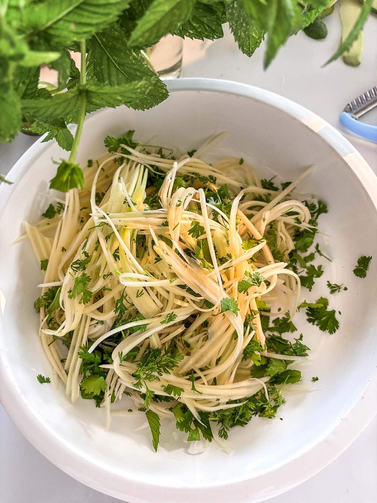 bowl of shredded green papaya with fresh herbs. 