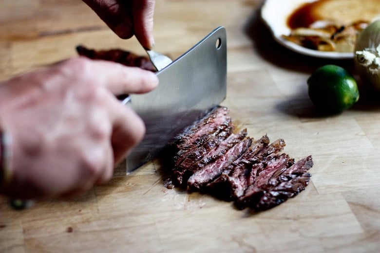 Grilled Steak being cut thinly on a cutting board.