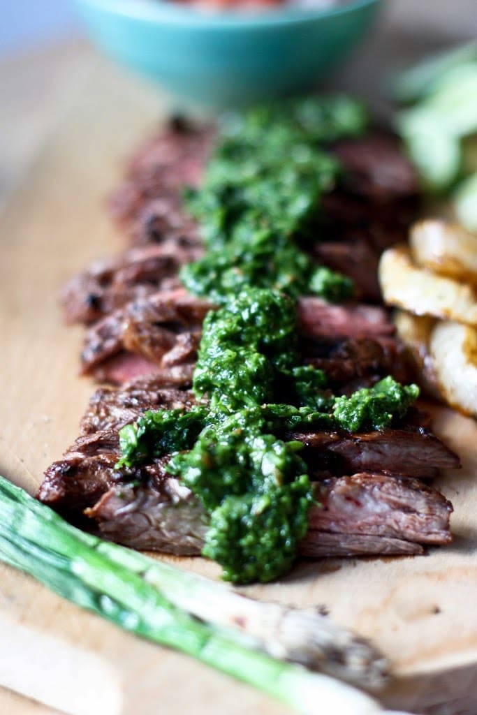 Grilled flank steak on a cutting board, thinly sliced with Chimichurri 