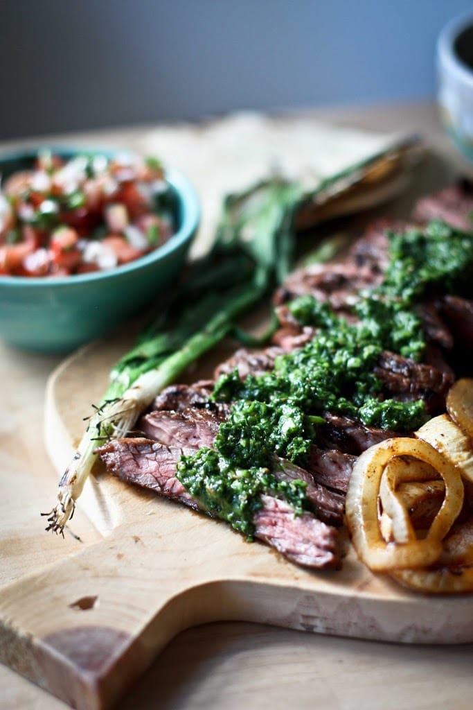 Carne Asada Recipe Grilled Flank Steak, thinly sliced on a cutting board with Chimichurri sauce