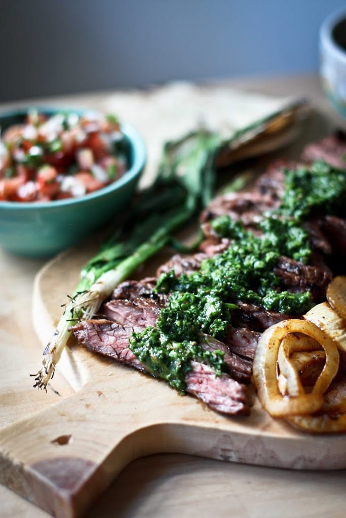 Grilled Flank Steak, thinly sliced on a cutting board with Chimichurri sauce 