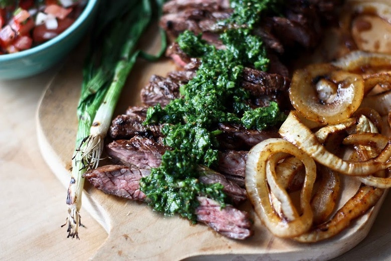 Grilled Steak Tacos, sliced on a cutting board with grilled onions, grilled scallions and Chimichurri Sauce