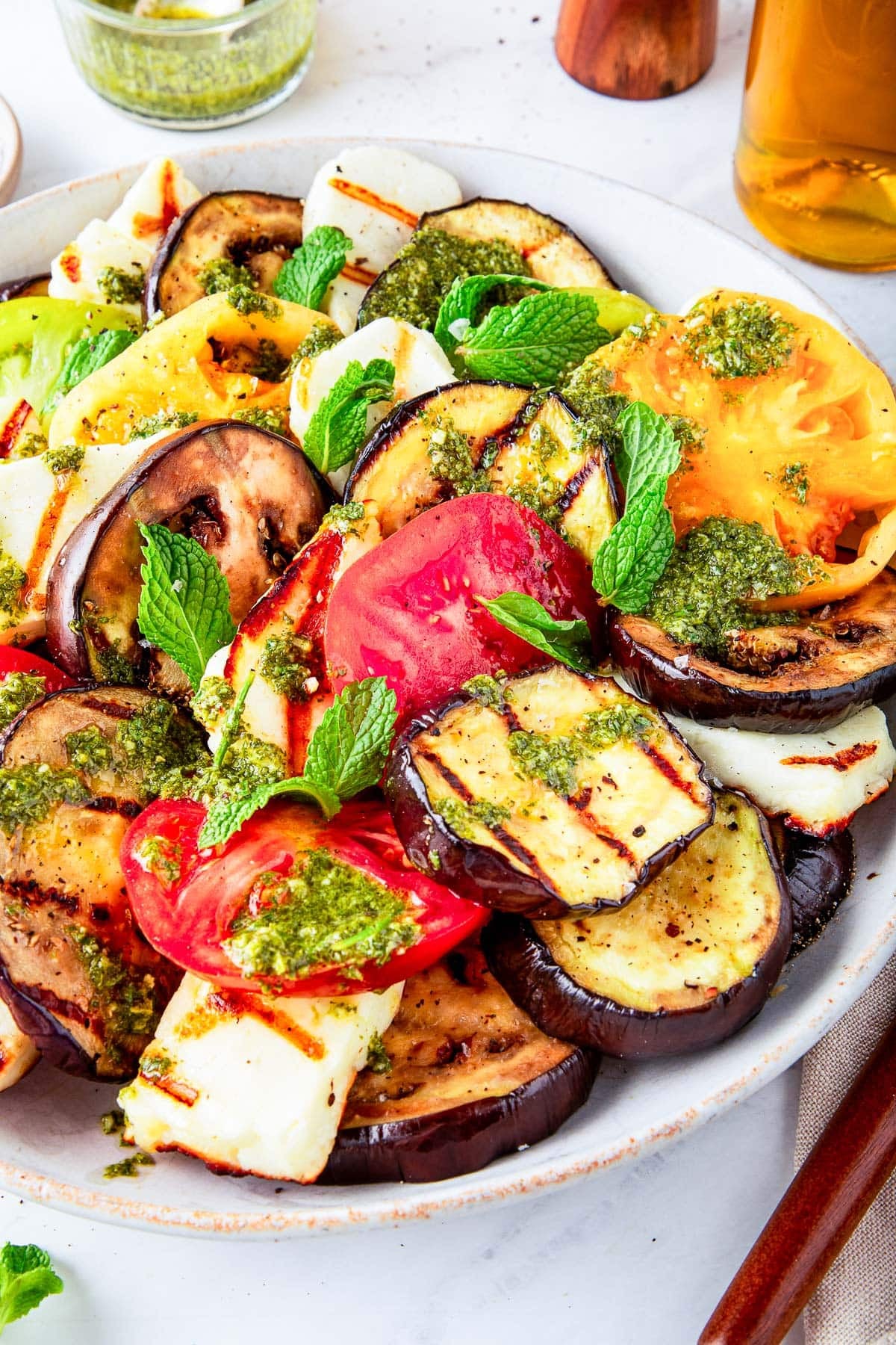plate of grilled halloumi cheese and grilled eggplant and heirloom tomatoes with mint dressing and fresh mint leaves.