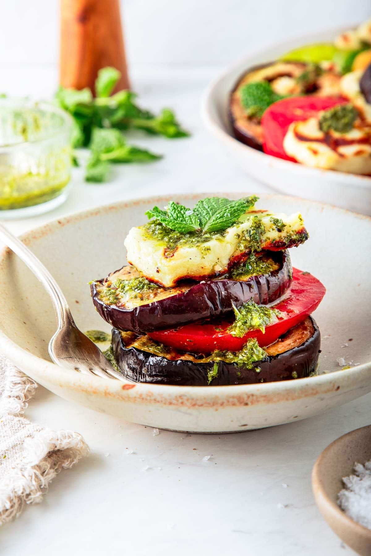 stack of grilled halloumi cheese, eggplant, and tomato with a drizzle of lemon-mint dressing on plate with fork.