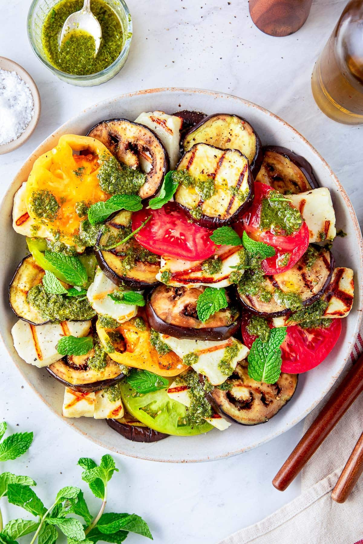 plate of grilled halloumi cheese with grilled eggplant and tomato slices, drizzled with mint dressing and fresh mint leaves.