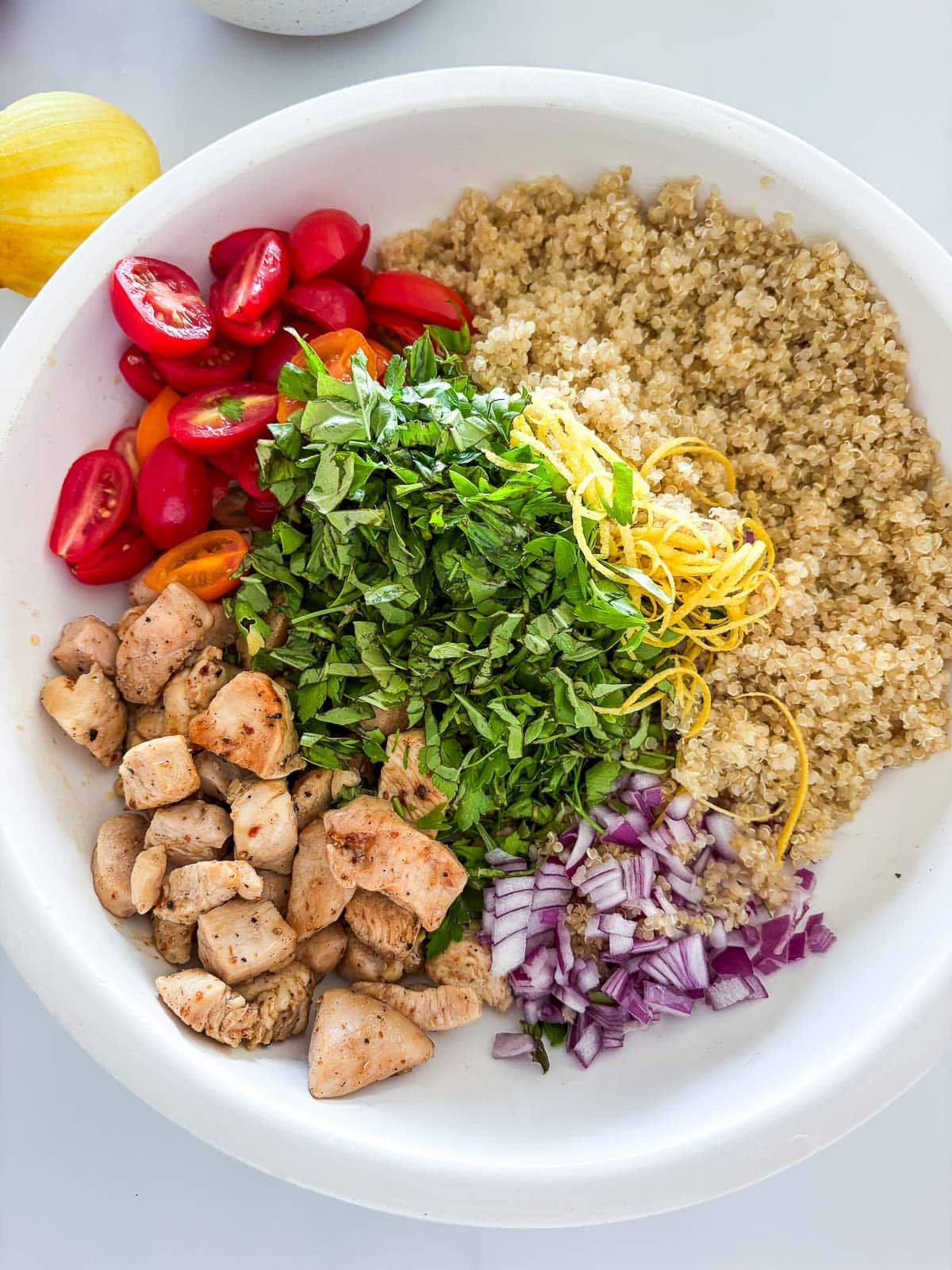 All the salad ingredients, seperated in a white bowl.