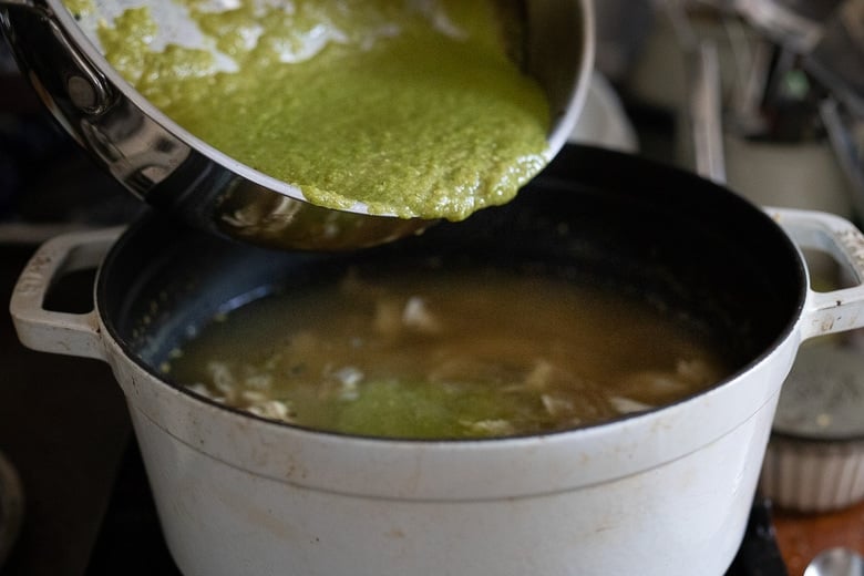 pouring the green sauce into the broth with the chicken