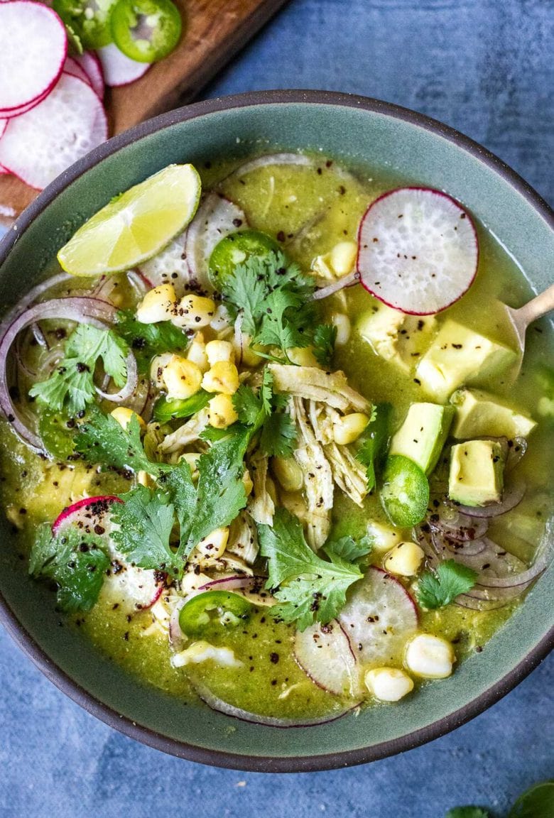 A delicious recipe for Pozole Verde- a flavorful Mexican stew made with tomatillos, green chilies, chicken and hominy, topped with cilantro, avocado and red onions. #pozole