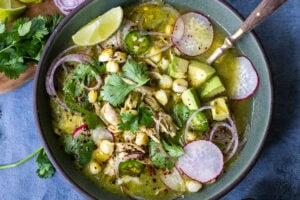 A delicious recipe for Pozole Verde- a flavorful Mexican stew made with tomatillos, green chilies, chicken and hominy, topped with cilantro, avocado and red onions. #pozole