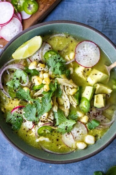 A delicious recipe for Pozole Verde- a flavorful Mexican stew made with tomatillos, green chilies, chicken and hominy, topped with cilantro, avocado and red onions. #pozole