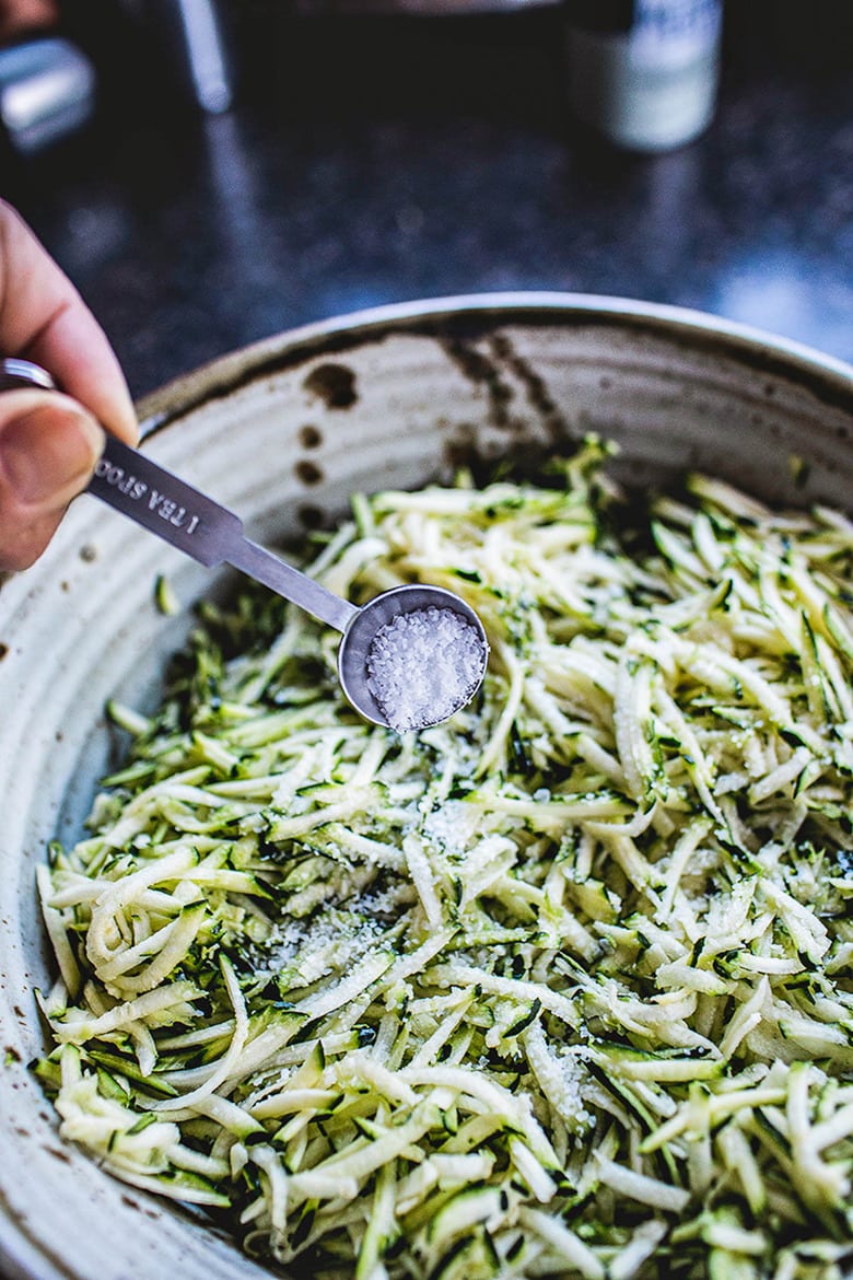 ceramic bowl with grated zucchini and teaspoon of kosher salt sprinkled over top.