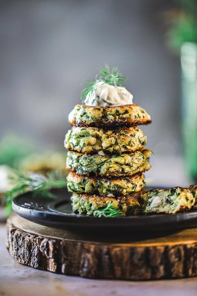stack of zucchini fritters on a plate topped with tzatziki and dill for a healthy summer dinner idea.