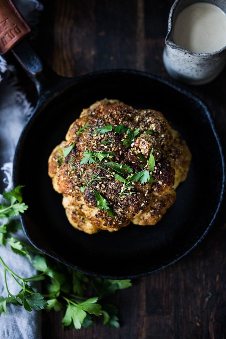 Whole Roasted Cauliflower with Zaatar Spice and Tahini Sauce- a healthy vegan side dish bursting with Middle Eastern flavor. Easy and delicious! #roastedcauliflower #cauliflower #veganside #tahinisauce #zaatar #tahinicauliflower