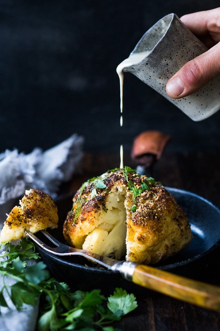 Whole Roasted Cauliflower with Zaatar Spice and Tahini Sauce- a healthy vegan side dish bursting with Middle Eastern flavor. Easy and delicious! #roastedcauliflower #cauliflower #veganside #tahinisauce #zaatar #tahinicauliflower