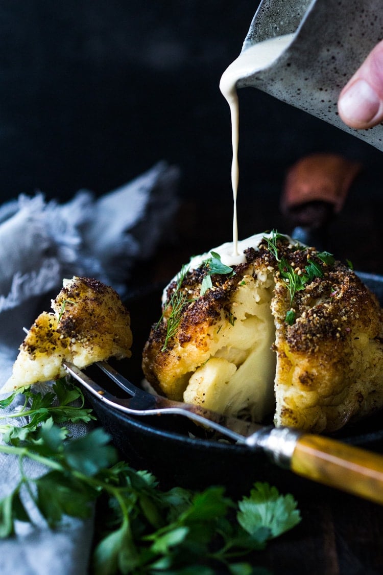 Whole Roasted Cauliflower with Zaatar Spice and Tahini Sauce- a healthy vegan side dish bursting with Middle Eastern flavor. Easy and delicious! #roastedcauliflower #cauliflower #veganside #tahinisauce #zaatar #tahinicauliflower