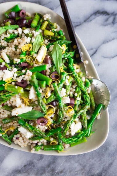 This Asparagus Salad recipe is easy, zesty, and bright! Made with fresh spring asparagus, pearl couscous, kalamata olives, pine nuts, feta, lemon zest, and mint all tossed in a lemony dressing. Vegan-adaptable.
