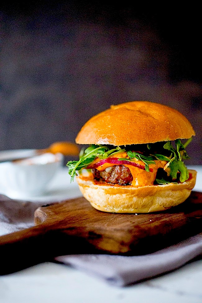 Grilled Lamb Burgers with Harissa Aioli, on a cutting board, completely assembled.