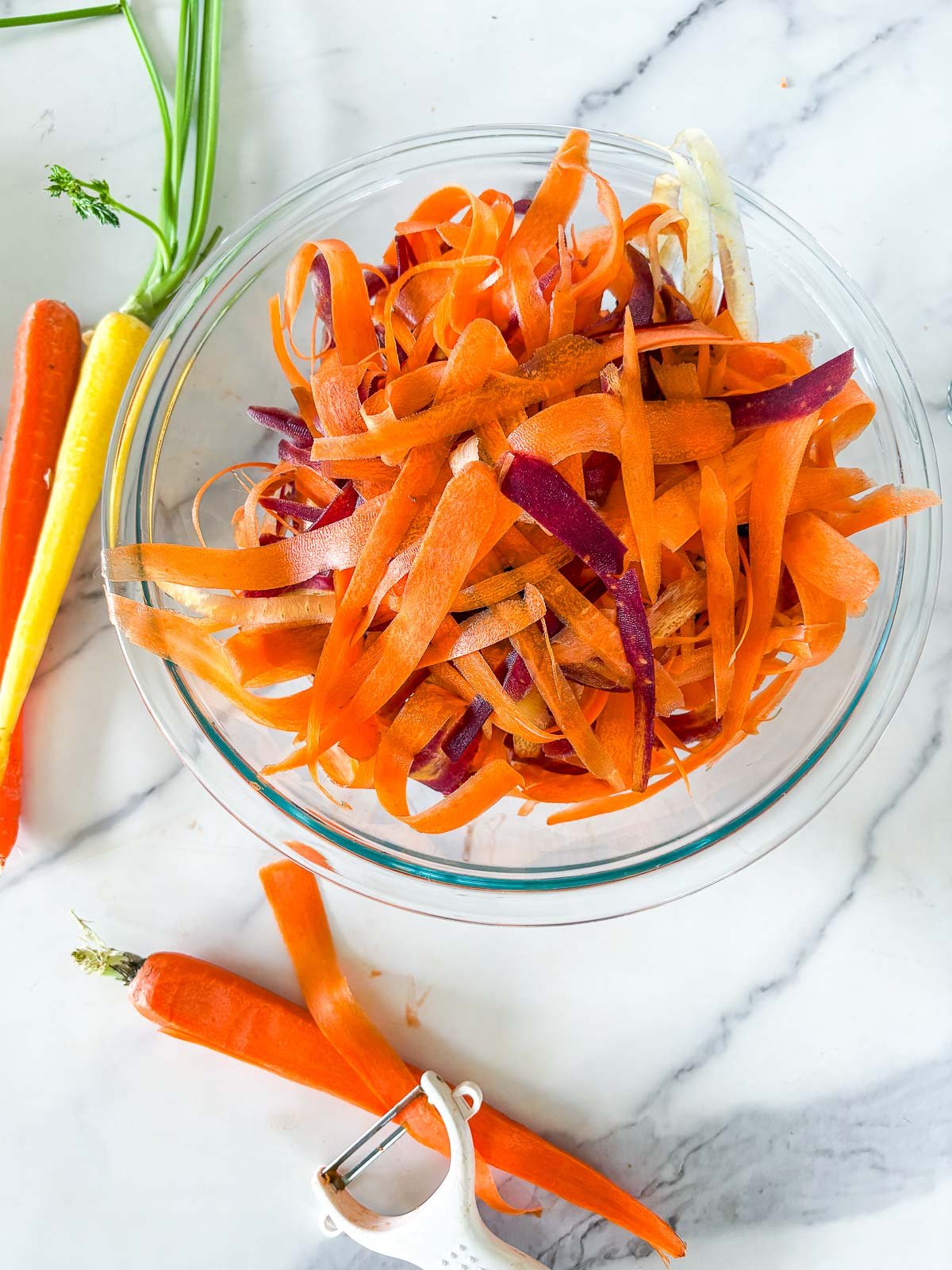 shaving the carrots with a vegetable peeler into a large bowl.