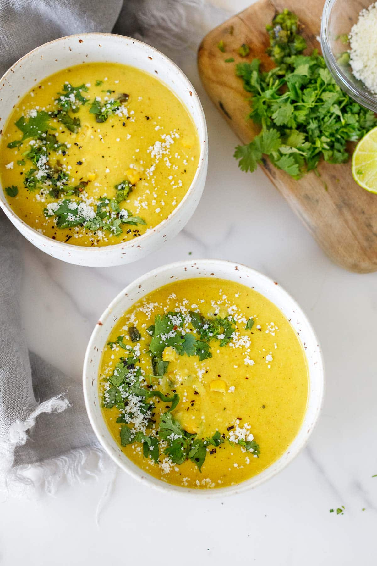 Creamy corn soup in white bowls with cotija cheese, lime, cilantro and jalapeno. 