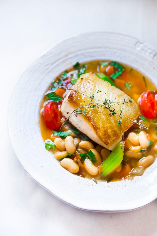 A simple healthy Mediterranean recipe for Sea Bass served over a fragrant Cannellini Bean Stew. Hearty and flavorful this easy dinner can be made in 30 minutes!  #seabass #cannellinibeans