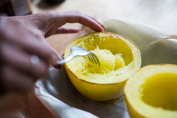 scooping out the cooked spaghetti squash into a bowl.