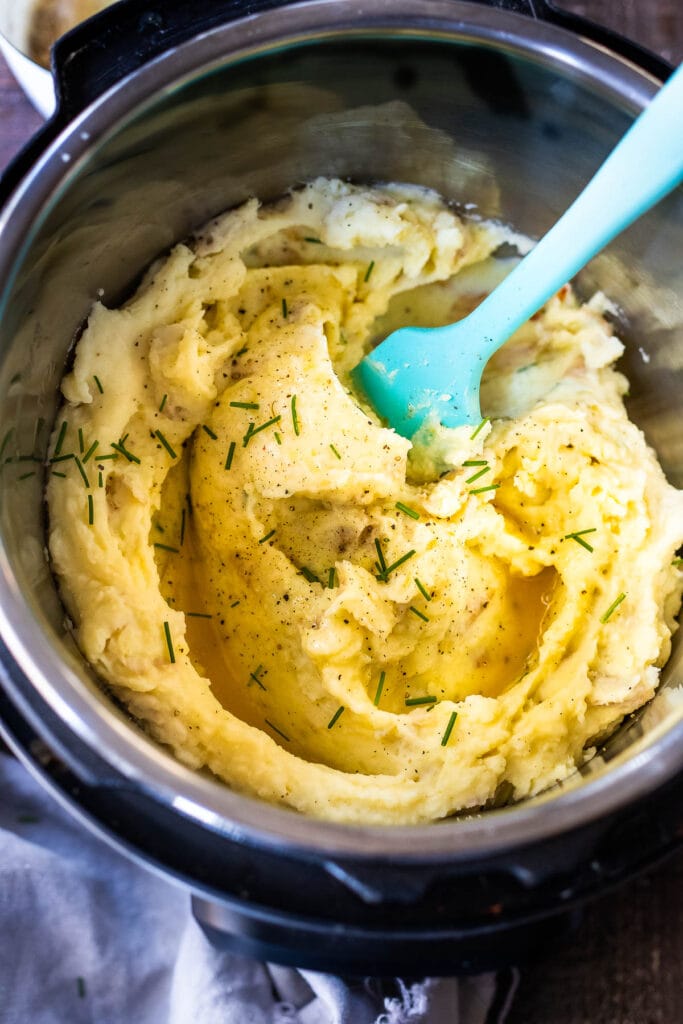 Instant Pot Mashed potatoes in pot with fresh chives with blue silicone spatula.