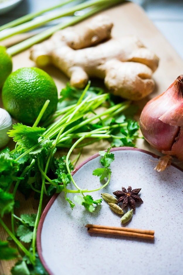 some ingredients for the Thai coconut sauce for turkey meatballs - star anise, cinnamon stick, and cardamom pods on a plate, fresh cilantro bunch, shallot, ginger, and limes.