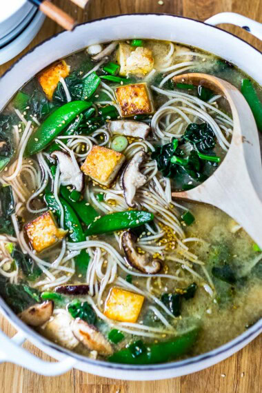 Asian noodle soup with soba noodles, shiitake, crispy tofu, snow peas, and sesame seeds in pot.