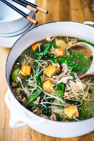 Asian noodle soup with soba noodles, shiitake, crispy tofu, snow peas, and sesame seeds in pot.