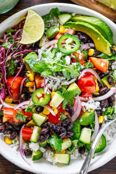 Our favorite burrito bowl recipe is made with seasoned black beans and rice topped with fresh tomatoes, avocado, corn, shredded cabbage, and a vegan cilantro lime crema.