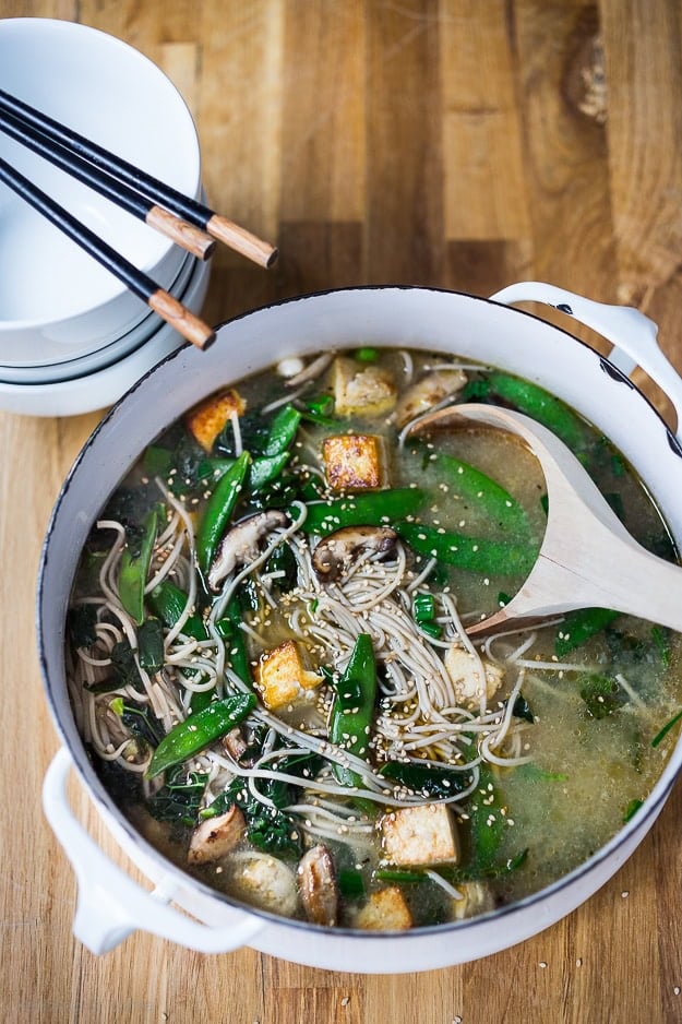 Soba Noodle Soup with Shiitakes, snow peas and tofu. Vegan and GF |www.feastingathome.com pot of Asian noodle soup with crispy tofu, soba noodles, greens, snap peas, and sesame seeds, with wooden ladle.