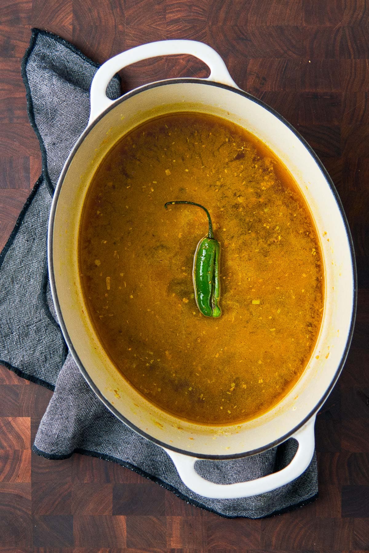 large dutch oven with sweet potato soup broth with serrano chili in the center, cut in half, stem intact.