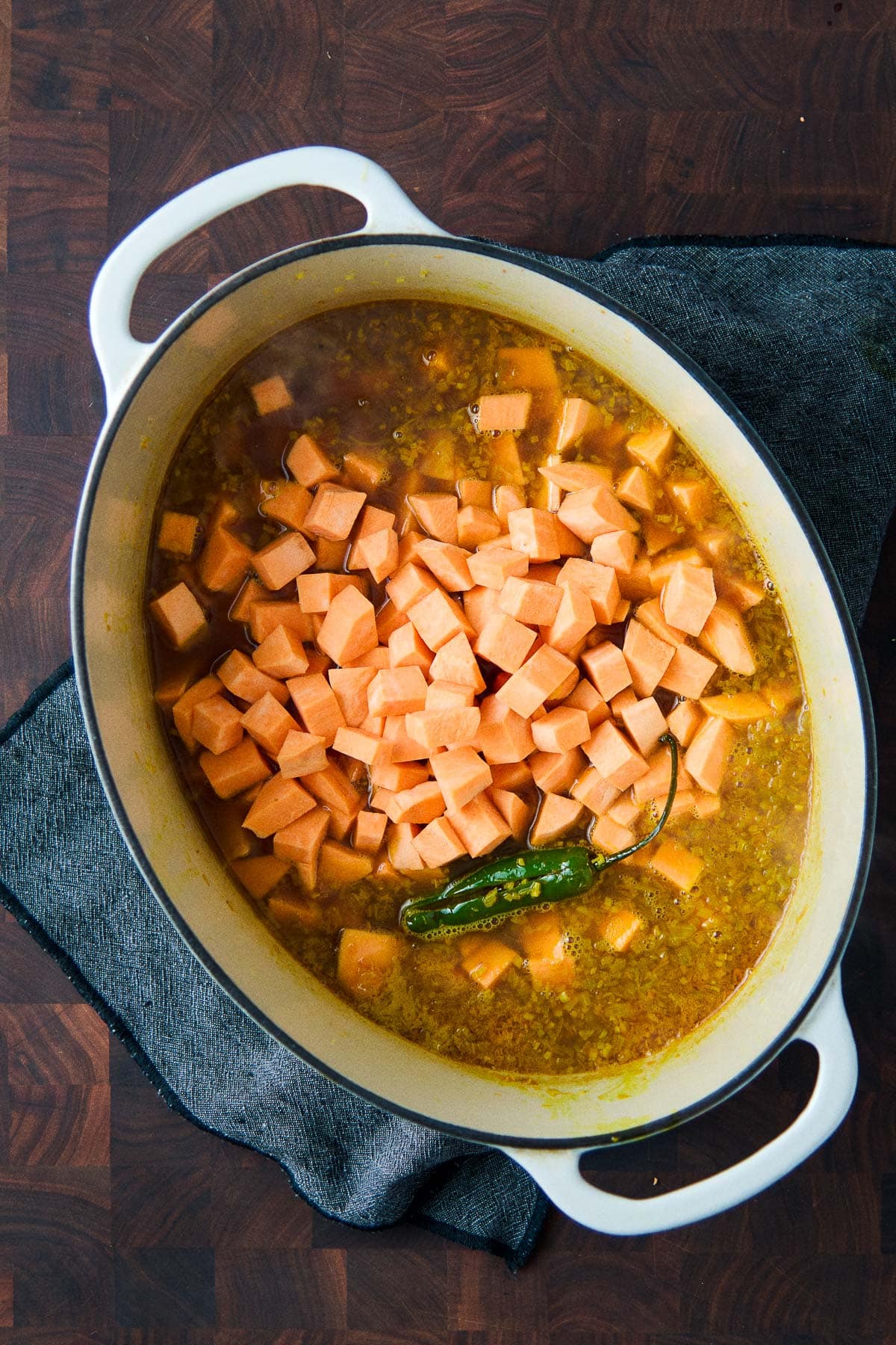 large dutch oven with uncooked sweet potato added with broth and serrano chili.
