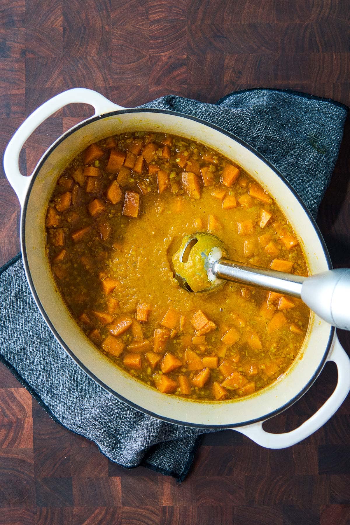large dutch oven with immersion blender puréing sweet potato soup. 