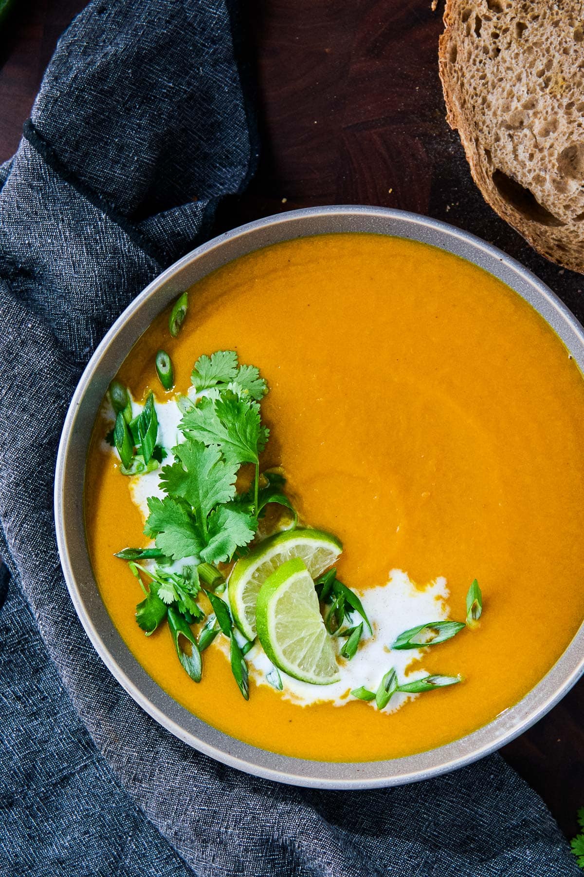 bowl of sweet potato soup with coconut milk, lime slices, cilantro, and scallions. 